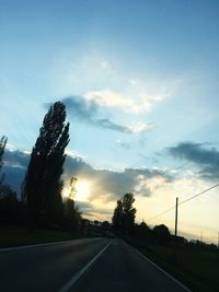 Road by trees against sky during sunset