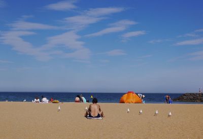 Rear view of shirtless man relaxing at beach against sky