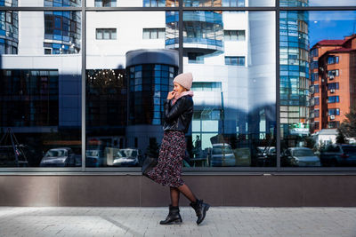 Young female student in warm autumn clothes coming out of the house with a backpack