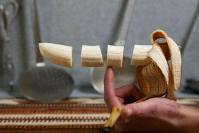 Cropped hand balancing banana slices on finger at home