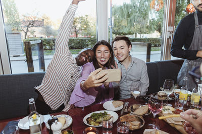 Woman taking selfie with male friends while celebrating in bar afterwork