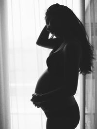 Side view of woman standing against window at home