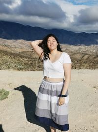 Beautiful young woman standing on mountain against sky