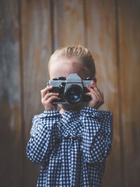 Close-up of girl photographing with camera against wall