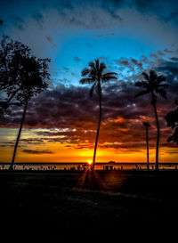 Silhouette palm trees on field against sky during sunset