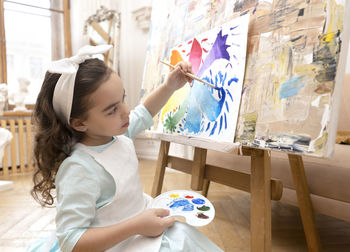 Cute girl drawing with a paint palette and a paintbrush. little painting artist.