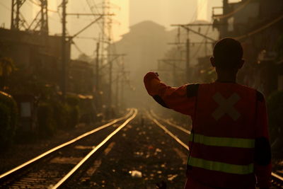 Rear view of manual worker with arms raised standing on railroad tracks