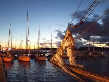 Boats moored in harbor at sunset