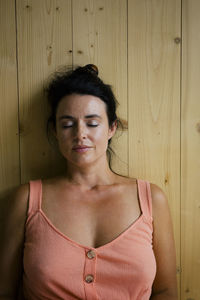 Relaxed woman with eyes closed sitting near wooden wall at home