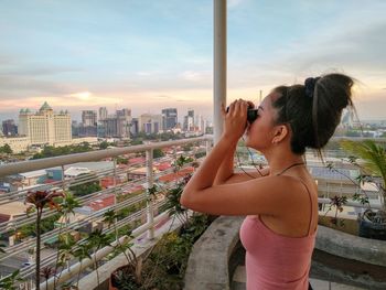 Young woman standing by cityscape against sky in city