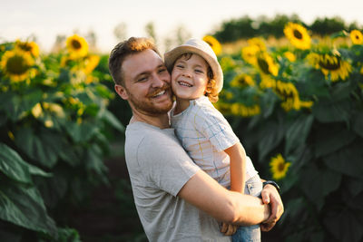 Father with little baby son in sunflowers field during golden hour. 