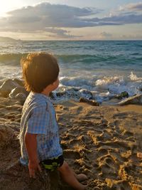 Side view of boy sitting on rock at beach during sunset