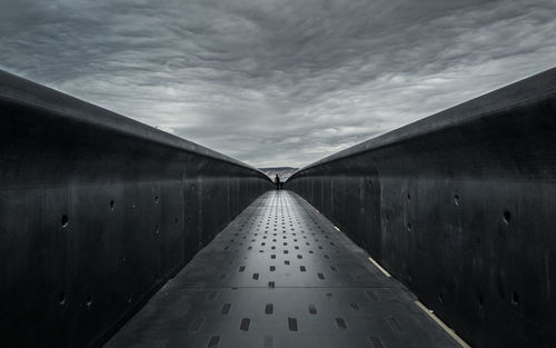 Narrow footbridge under cloudy sky