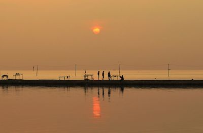 Silhouette sailboats in sea against orange sky