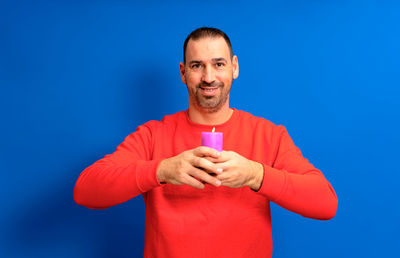 Portrait of man holding ice cream cone against blue background
