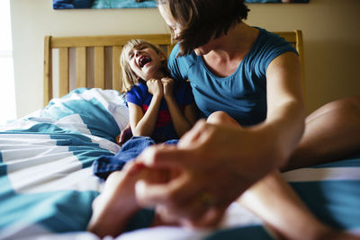 Mother tickling daughter's feet while sitting on bed