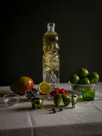 Fruits in glass bottle on table against black background