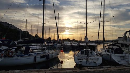 Boats moored in harbor at sunset