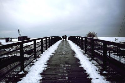 Footbridge against cloudy sky during winter