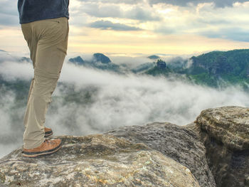 Legs in hiking trousers and leather trekking shoes on peak above misty valley. autumnal nature