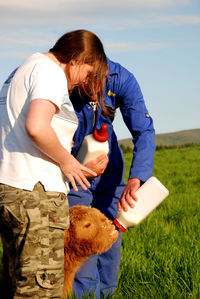 Man and woman feeding calf on field