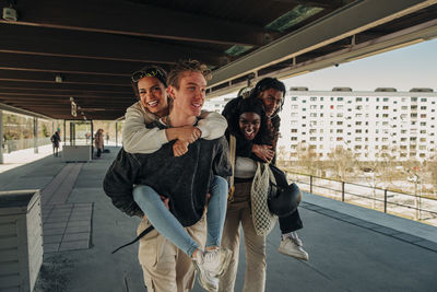 Multiracial playful friends piggybacking each other at railroad station platform