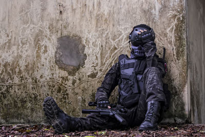 Full length of soldier sitting against old wall in forest