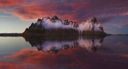 Scenic view of mountains by lake against dramatic sky during sunset