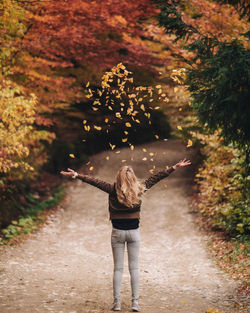 Rear view of woman throwing leaves on road during autumn