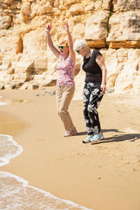 Two senior women walking along the rocky seashore and playing with the waves