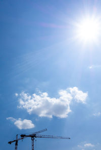 Low angle view of crane against blue sky on sunny day