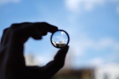 Cropped image of hand holding lens against sky