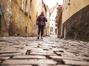 Rear view of woman walking on alley amidst buildings in city