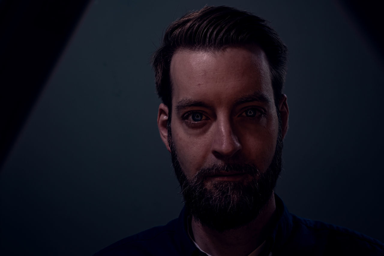 portrait, headshot, one person, beard, studio shot, facial hair, indoors, front view, looking at camera, young men, young adult, black background, close-up, men, males, focus on foreground, mid adult men, lifestyles, contemplation, human face