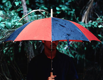 Man holding umbrella while standing by plants during rainy season