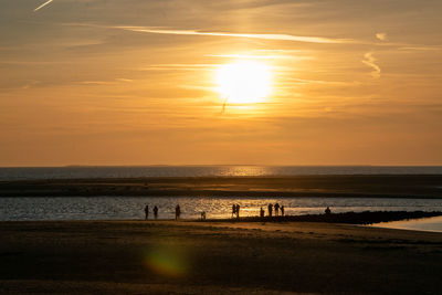 Silhouette people on beach against sky during sunset