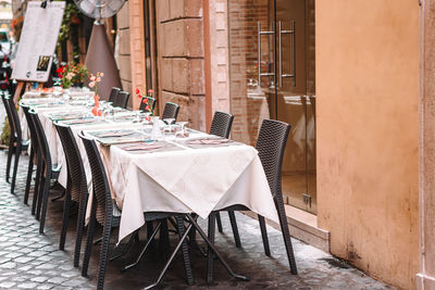 Empty chairs and tables at sidewalk cafe amidst buildings