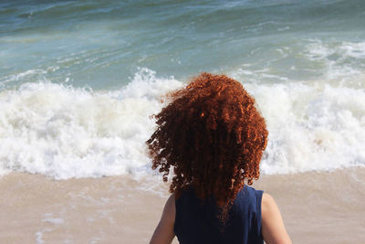 Rear view of woman with curly hair on shore at beach