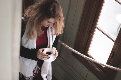 Young woman drinking coffee while standing by window