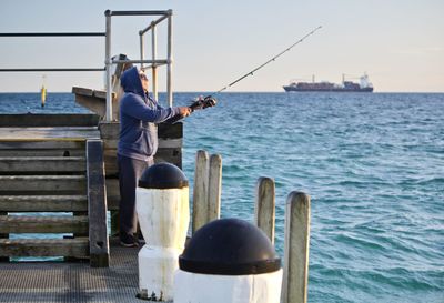 Man fishing in sea against sky