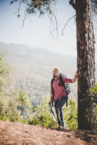 Man standing by tree trunk against sky