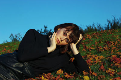 Portrait of young woman lying down on field against clear blue sky