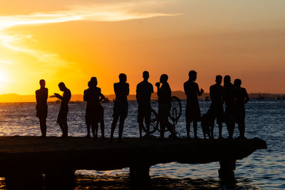 Young people and silhouettes are seen together during sunset having fun on top of the crush bridge 