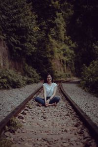 Woman sitting on railroad track amidst trees in forest