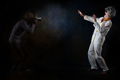 Midsection of man with arms outstretched against black background