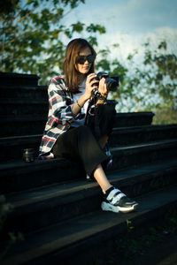 Young woman photographing while sitting on bench