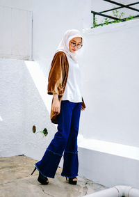 Full length portrait of woman standing against wall