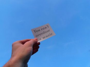 Close-up of cropped hand holding paper with message against clear blue sky