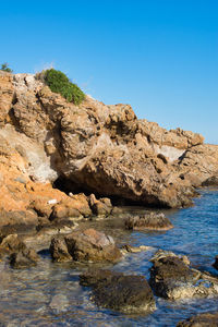 Rock formations by sea against clear blue sky