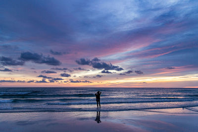 Woman standing on beach against sky during sunset